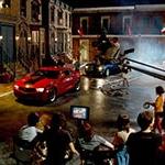 满帆大学's Backlot in the evening filled with a full film production crew shooting a scene featuring two muscle cars, 一个红的，一个黑的.